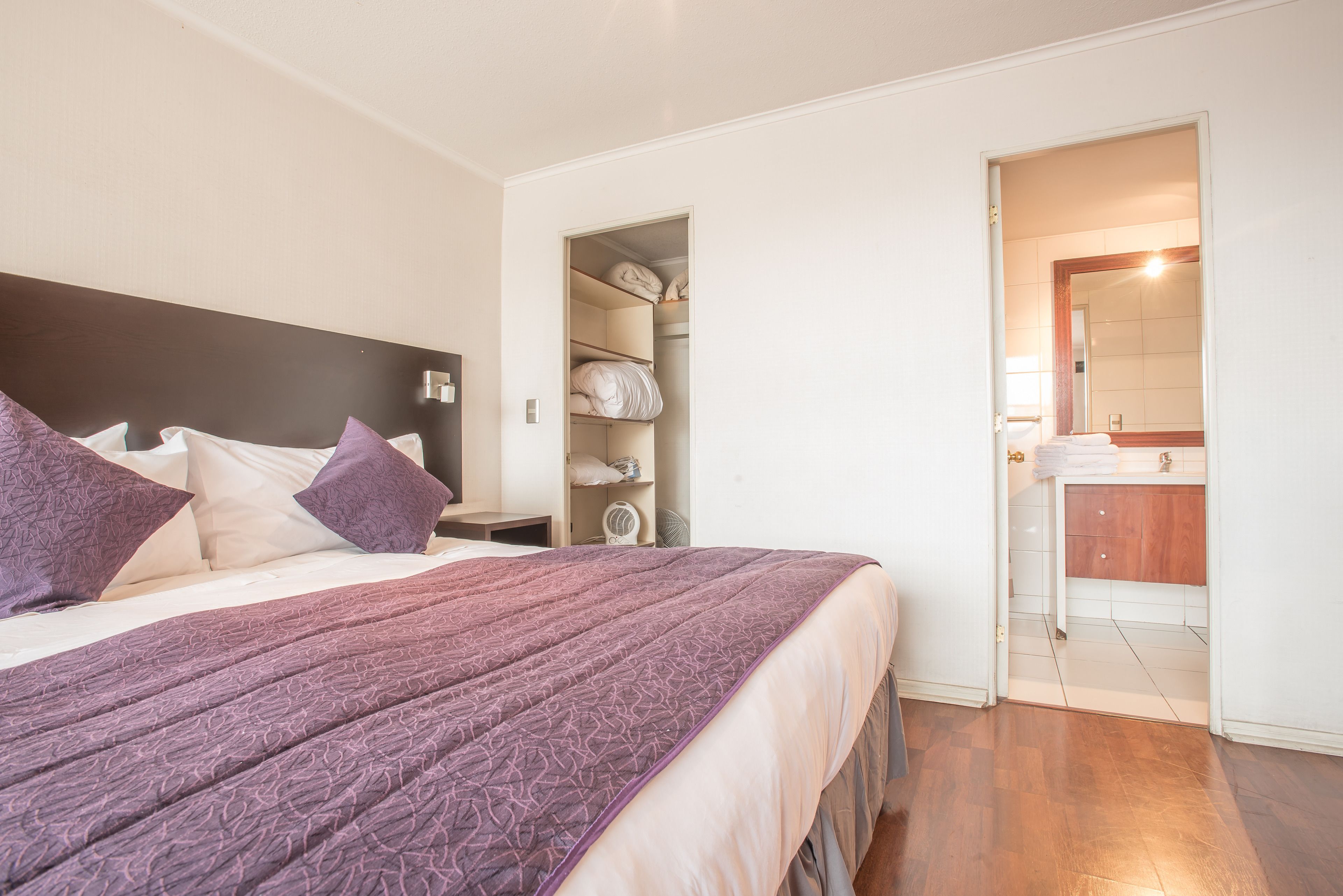 A bedroom with a bed, a nightstand, a closet, and a bathroom visible through an open door.