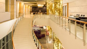 A modern hotel lobby with a glass railing, a staircase, and a reception area.