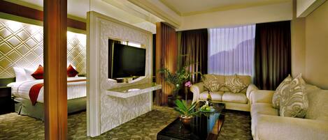 Habitación de hotel con cama, sofá, televisor y mesa de centro con planta.