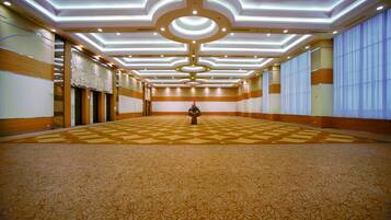 A spacious hotel lobby with a patterned carpet, a central floral arrangement, and a modern ceiling design.