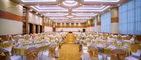 A banquet hall with rows of round tables, white tablecloths, and chairs with gold sashes.