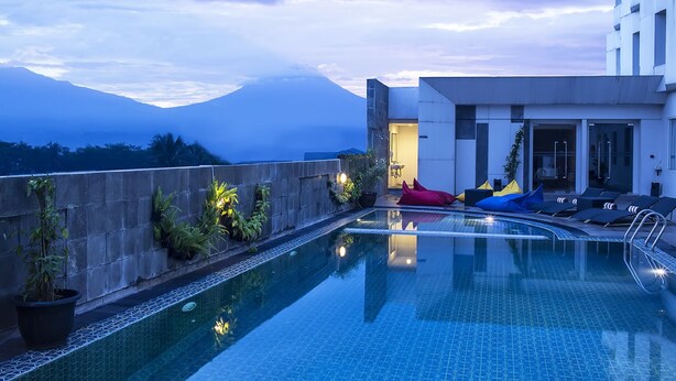 A rooftop pool with a view of a mountain, lounge chairs, and potted plants.