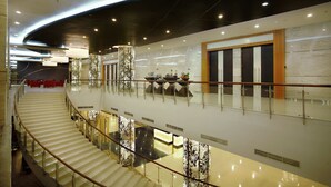 A modern hotel lobby with a curved ceiling, a glass railing, and a staircase leading to an upper level.