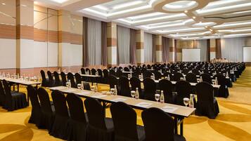 A conference room with rows of tables and chairs, a podium, and a large screen.