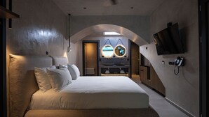 A modern bedroom with a large bed, a vanity with two mirrors, a flat-screen TV mounted on the wall, and a skylight above the vanity. - Royal Hotel and Suites (Kassandra)