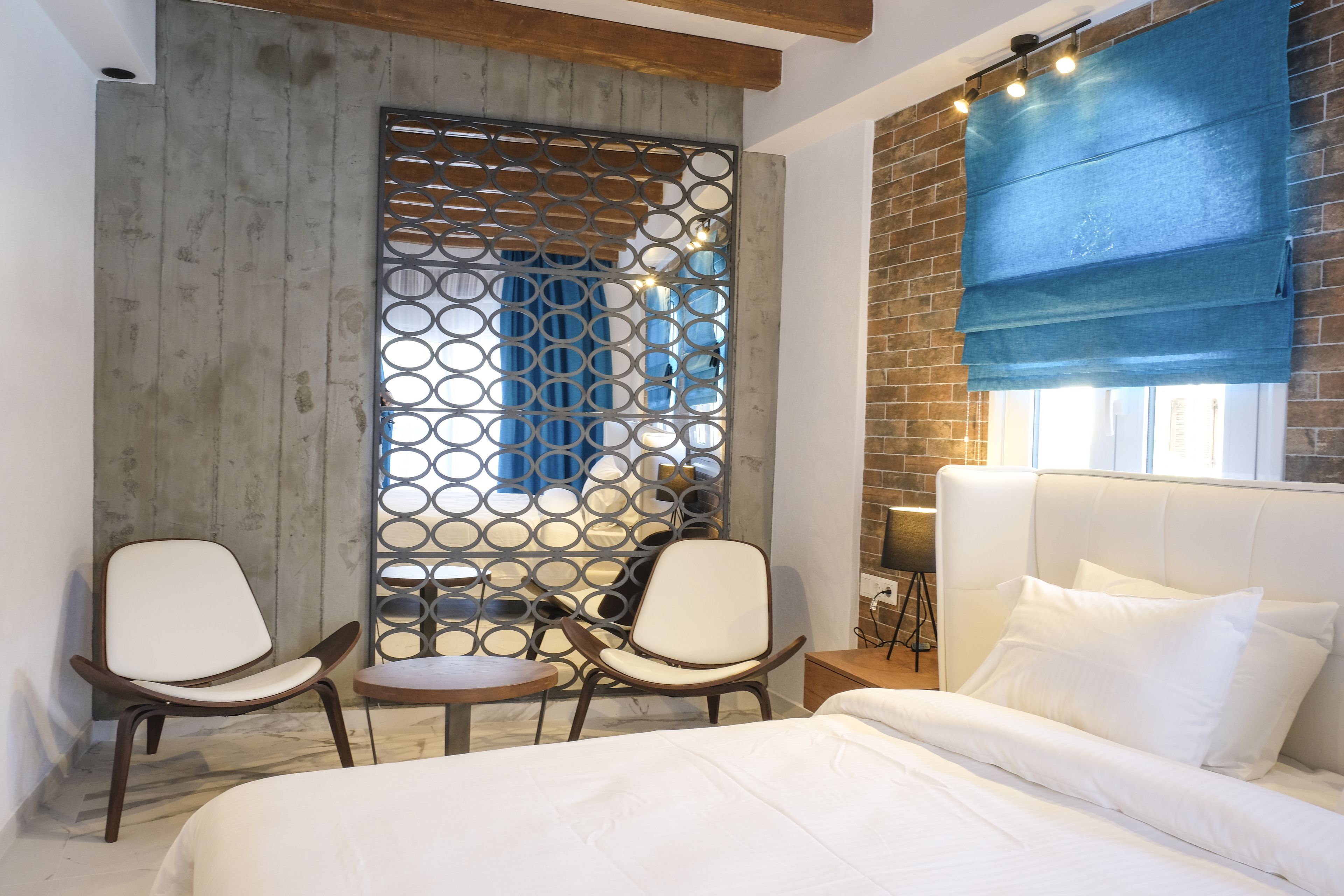 A modern hotel room with a large bed, two chairs, a small table, and a decorative partition.