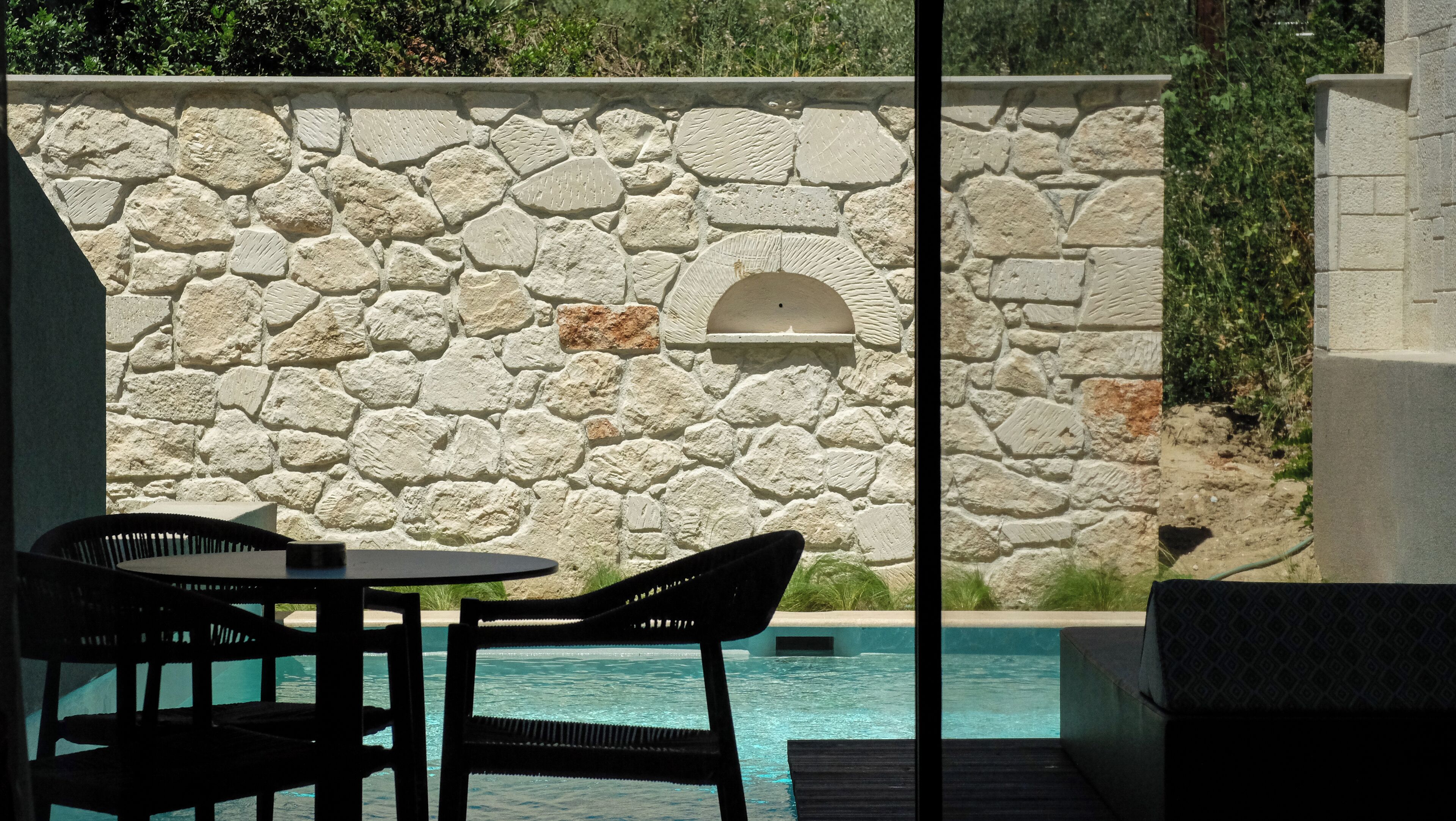 Un espace piscine agrémenté de murs en pierre, d’une petite fenêtre en arc de cercle et de mobilier d’extérieur.