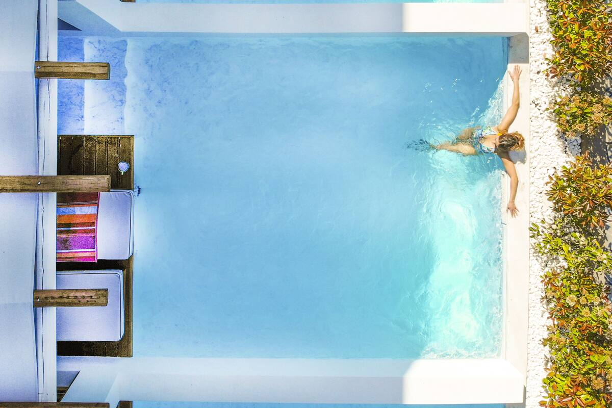 A pool with a wooden deck, lounge chairs, and a person swimming.