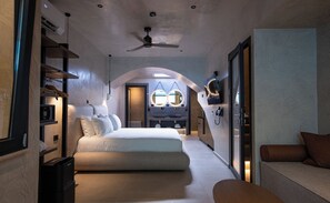 A modern hotel room with a bed, a sofa, a desk, and a bathroom with a mirror and sink. - Royal Hotel and Suites (Kassandra)