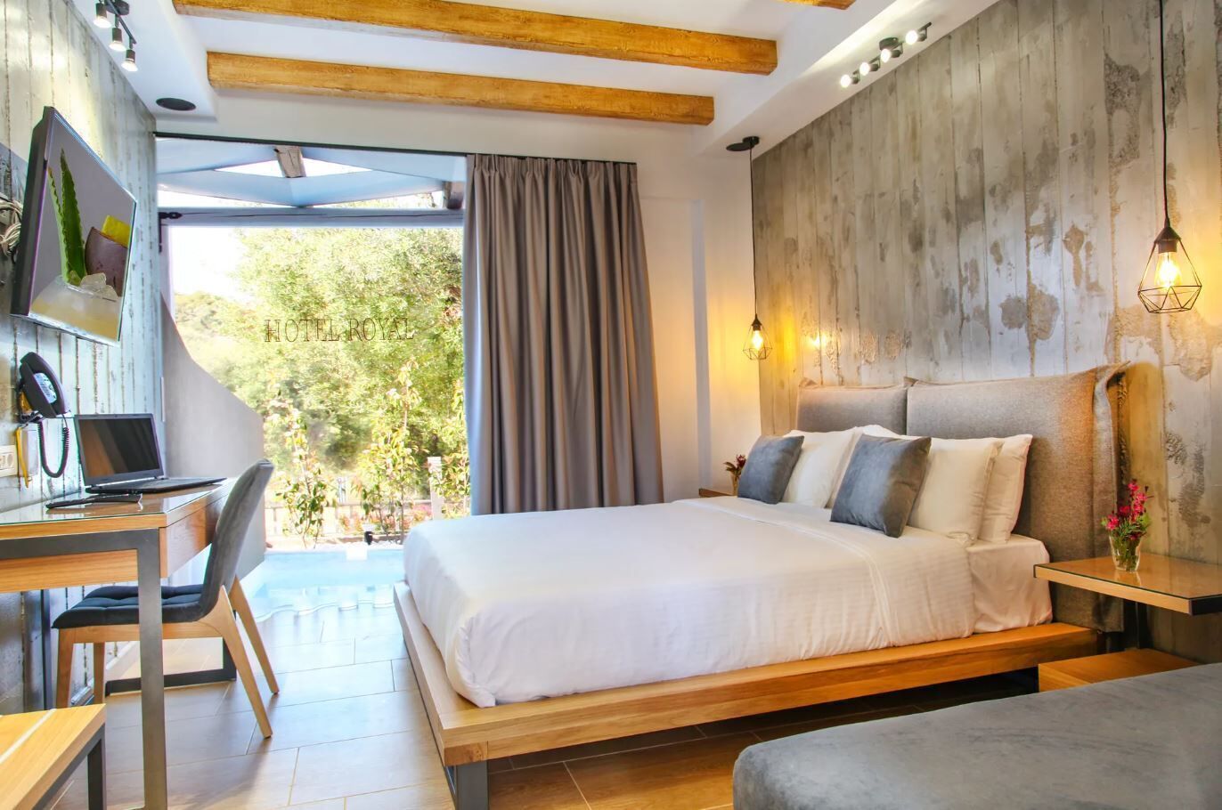 Une chambre d’hôtel moderne, dotée d’un lit, d’un bureau et d’une chaise, offrant une vue sur la verdure et agrémentée d’un mur au style rustique.