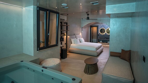 A modern bedroom with a large bed, a bathtub, and a seating area. - Royal Hotel and Suites (Kassandra)