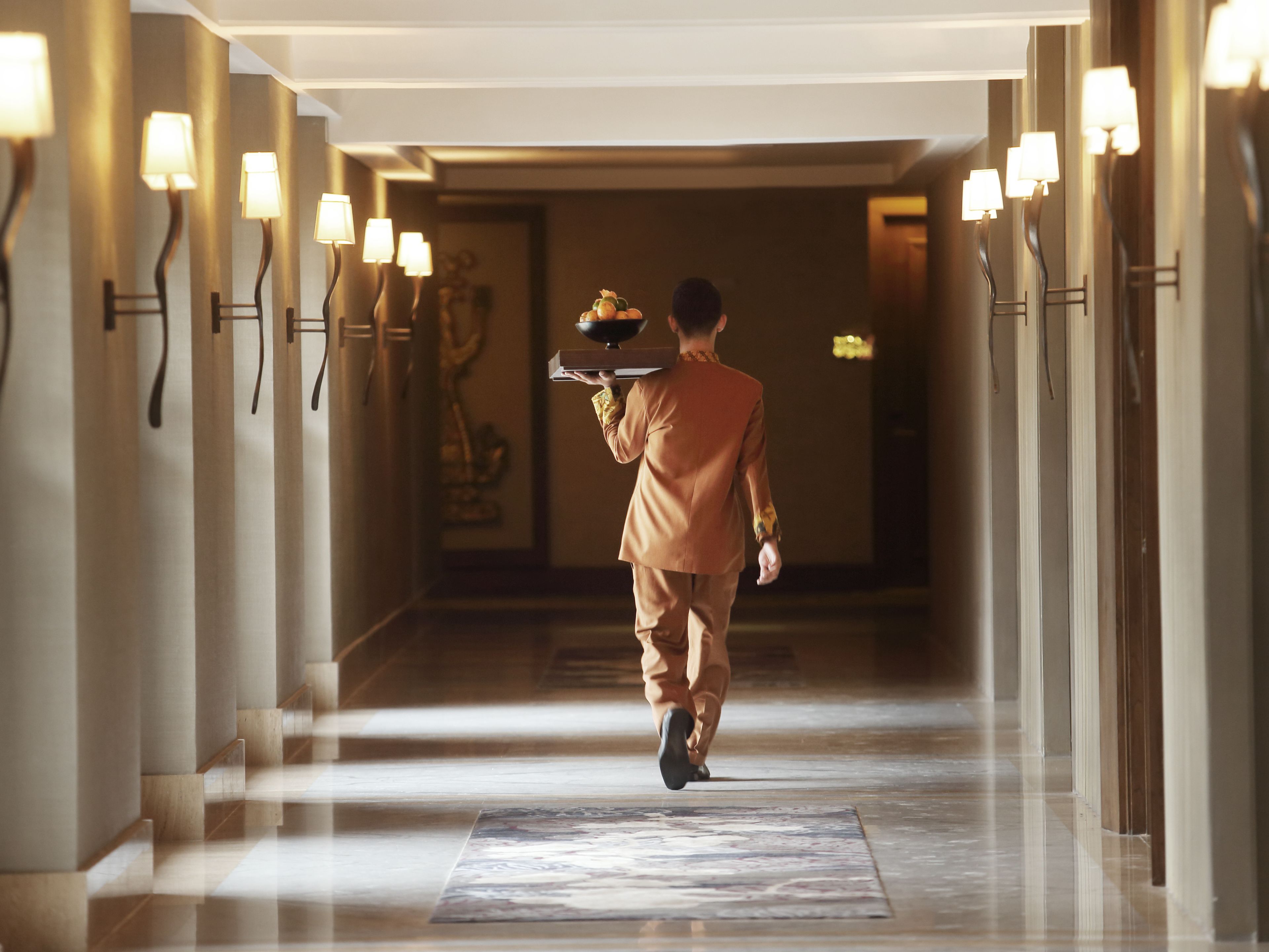 A hotel corridor with a person carrying a tray.
