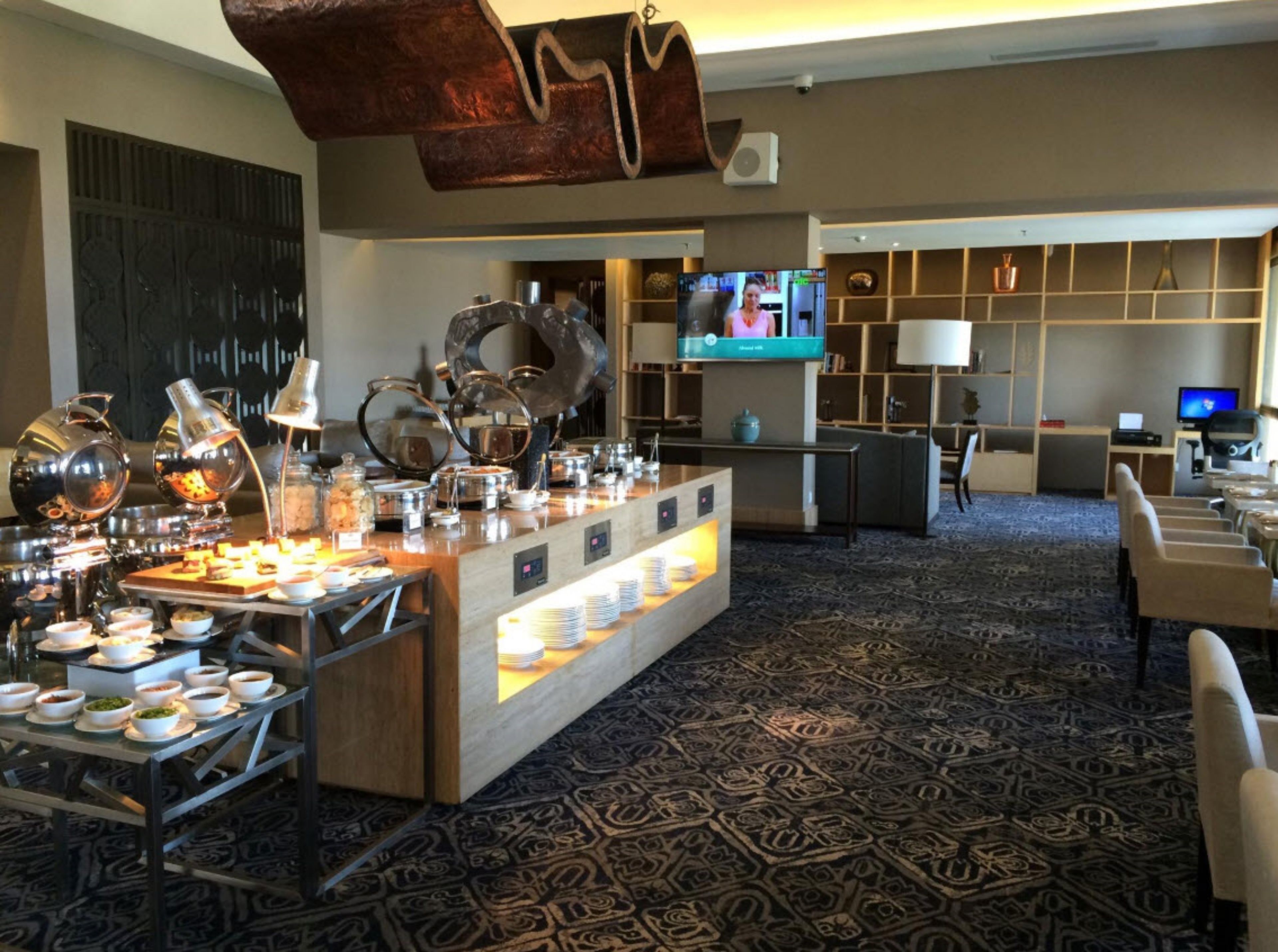A hotel lobby with a buffet area, seating, and a TV screen.