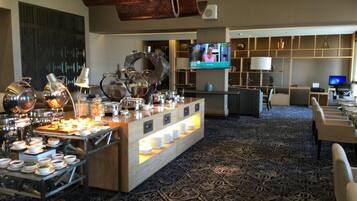 A hotel lobby with a buffet area, seating, and a TV screen.