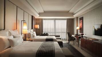 A hotel room with two beds, a desk, a chair, a TV, and a large window with curtains.
