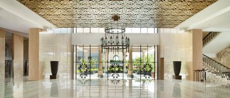 Un hall espacioso con suelo de mármol reflectante, techo decorativo y un gran candelabro.