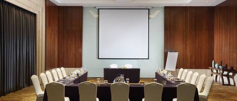 A conference room with a large table, chairs, a projector screen, and a whiteboard.