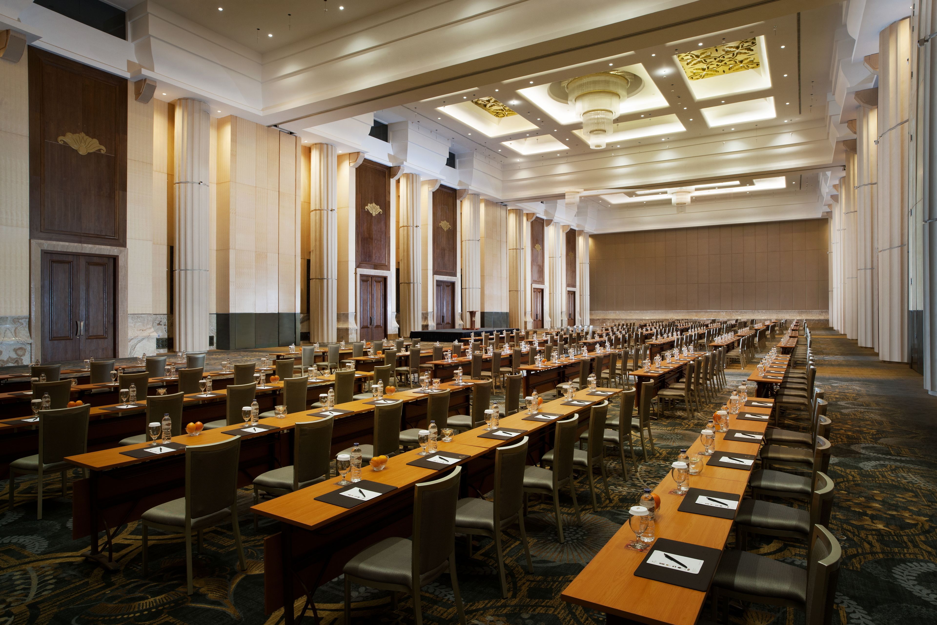 A large conference room with long tables, chairs, and a stage.