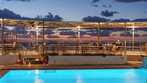 A rooftop pool area with a view of the sunset, lounge chairs, and a covered seating area. - Dedalos Beach Hotel (Rethymno)
