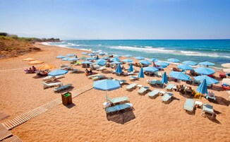 Una playa con numerosas tumbonas y sombrillas, un pasillo de madera y el océano al fondo.