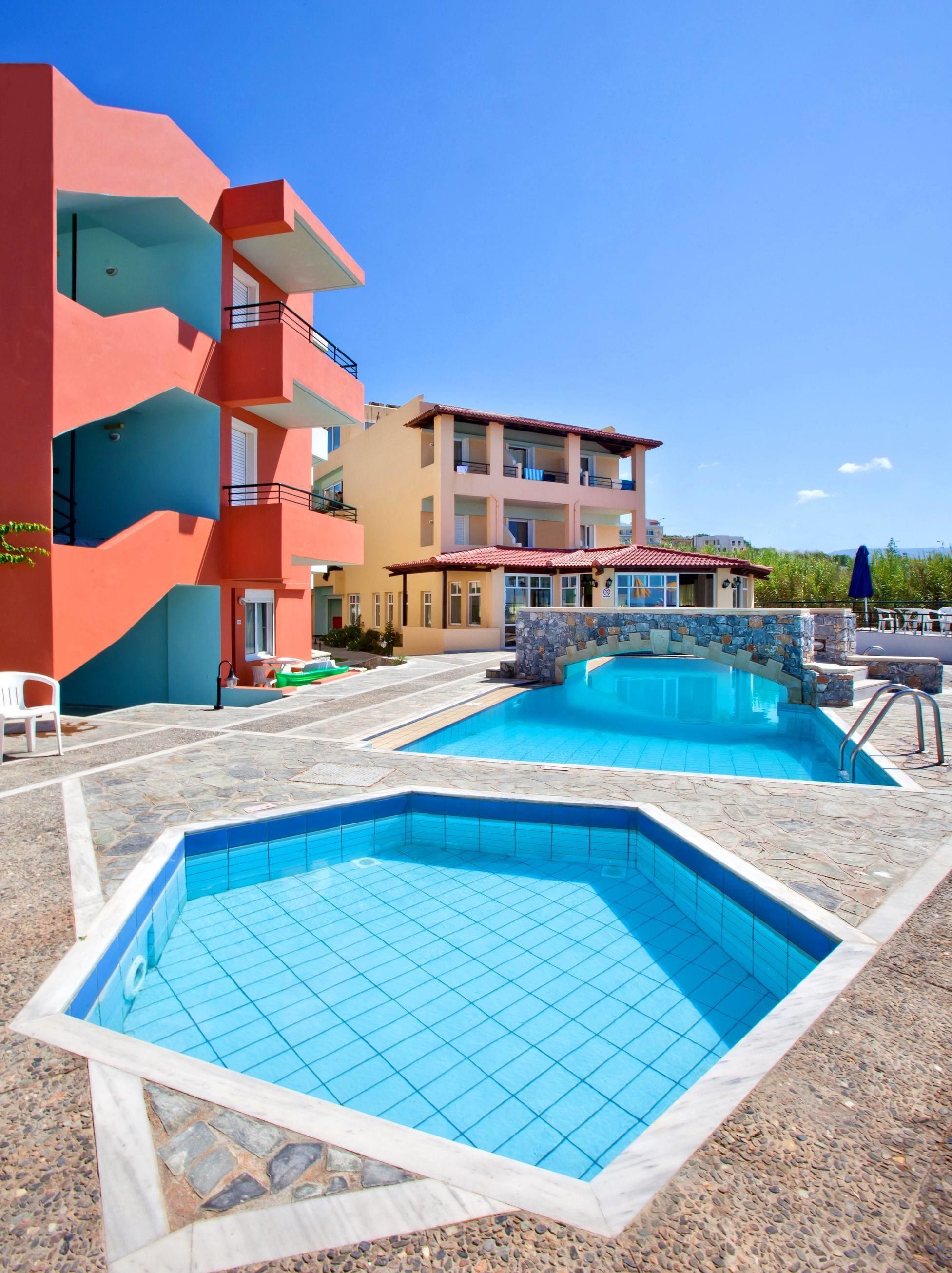 A hotel with a swimming pool, a red building, and a beige building with balconies.