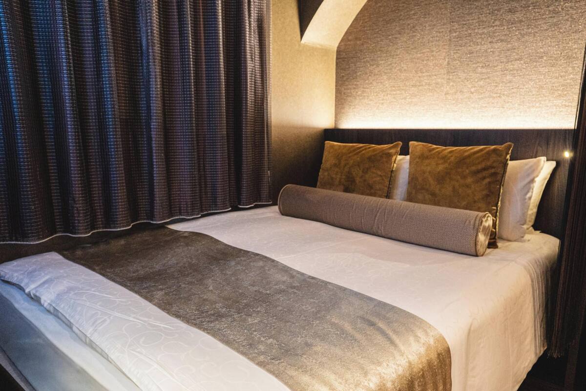 Een net opgemaakt bed met een wit-bruin dekbed, twee kussens en een hoofdbord met een lamp.