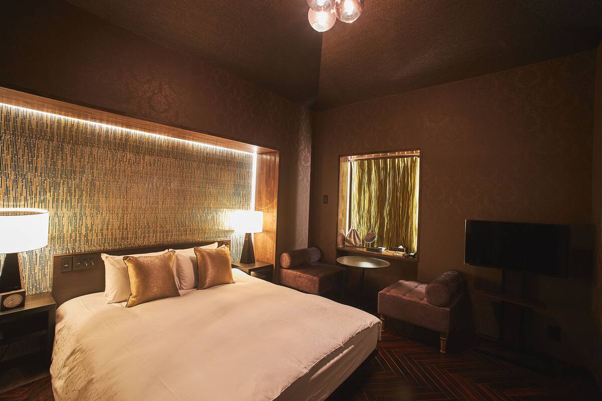 Een hotelkamer met een groot bed, nachtlampjes, een klein tafeltje, een stoel, een televisie en een behang met een patroon.