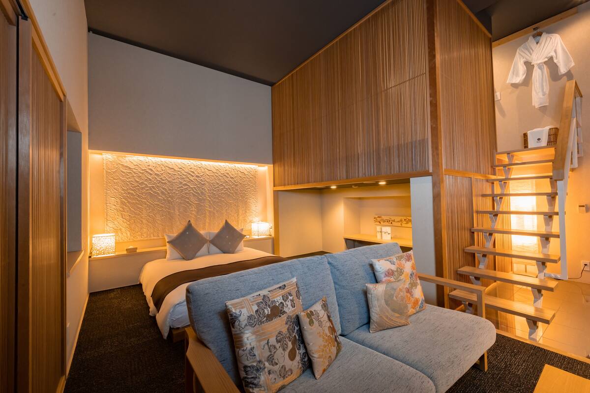Een moderne hotelkamer met een bed, een bank, een houten garderobe en een trap.