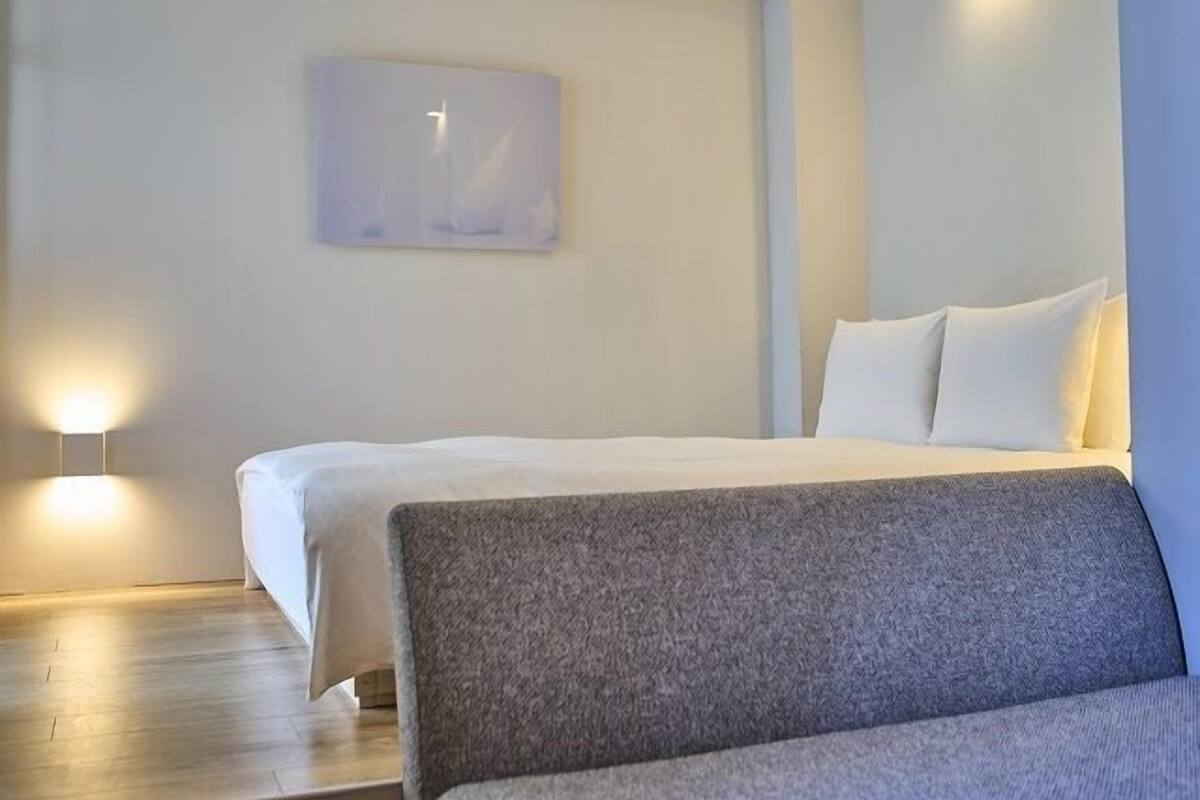 Een moderne hotelkamer met een bed, een bankje en wandlampen.