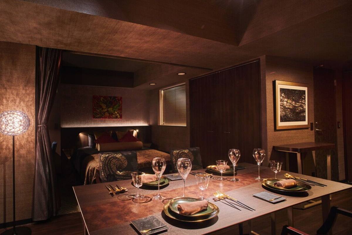 Een eetgedeelte met een lange tafel gedekt voor een maaltijd, een bank op de achtergrond en kunstwerken aan de muren.