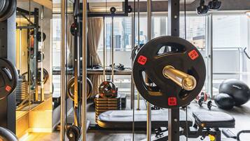 A gym with weightlifting equipment, a bench, and a window with a city view.