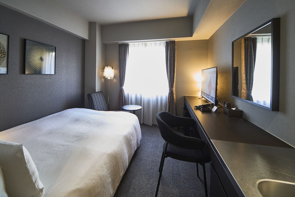 Een hotelkamer met een bed, bureau, stoel, televisie en een raam met gordijnen.