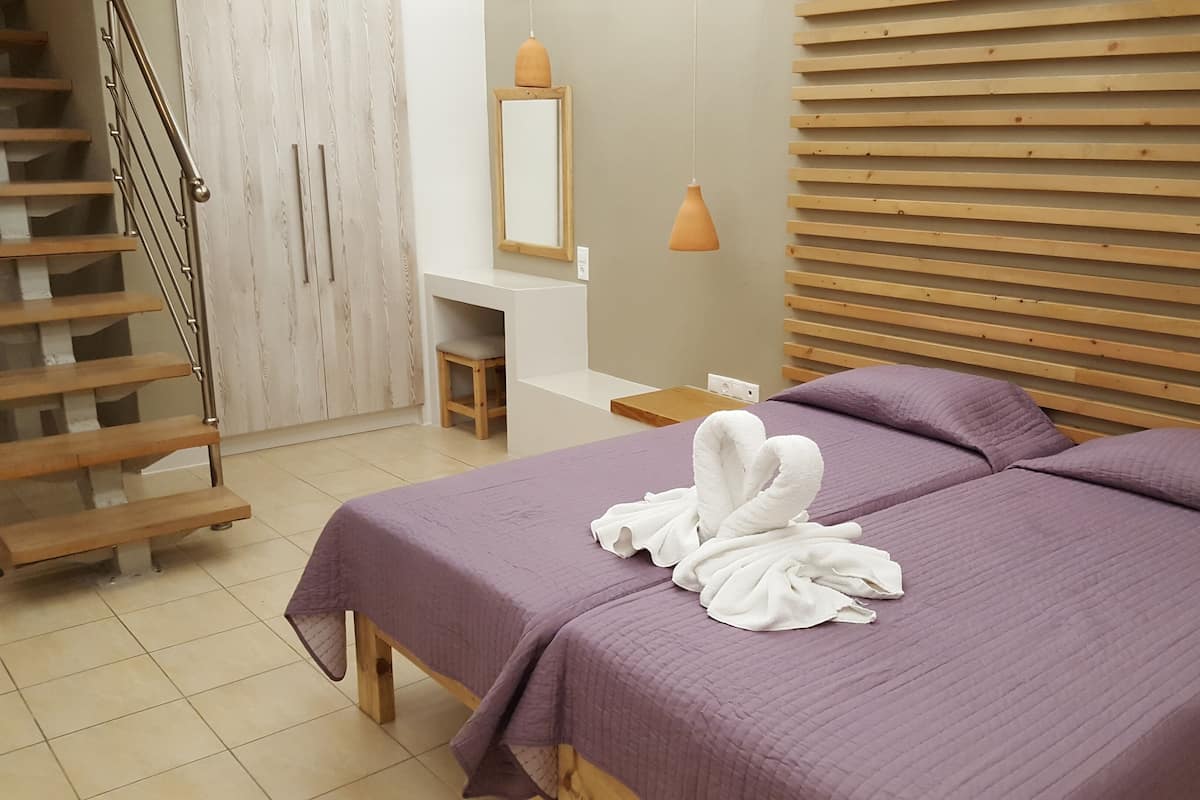 A bedroom with two beds, a wooden staircase, a small stool, a mirror, and a pendant light.