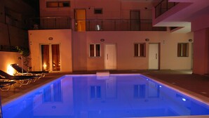 A swimming pool with lounge chairs and a building with multiple doors and windows. - Blue Sky Apartments (Rethymno)