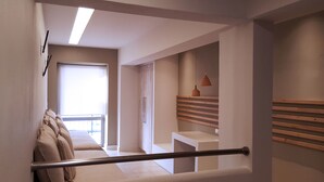 A modern hotel corridor with a bed, a wooden bench, and a hanging pendant light. - Blue Sky Apartments (Rethymno)