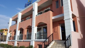 A hotel with a pink facade, multiple balconies, and a staircase leading to the entrance. - Blue Sky Apartments (Rethymno)