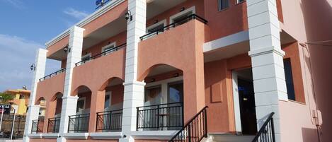 Un hôtel à la façade rose, doté de nombreux balcons et d’un escalier menant à l’entrée.