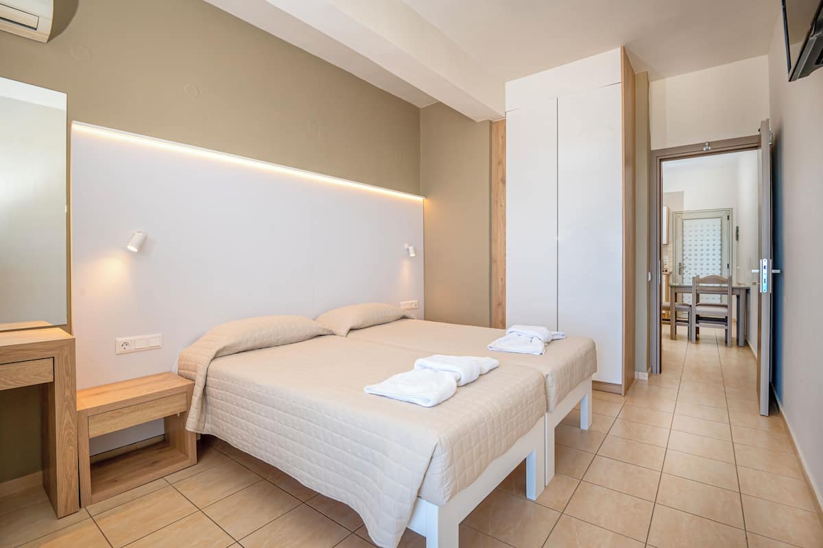A hotel room with two beds, a bedside table, a wardrobe, and a bathroom visible in the background.
