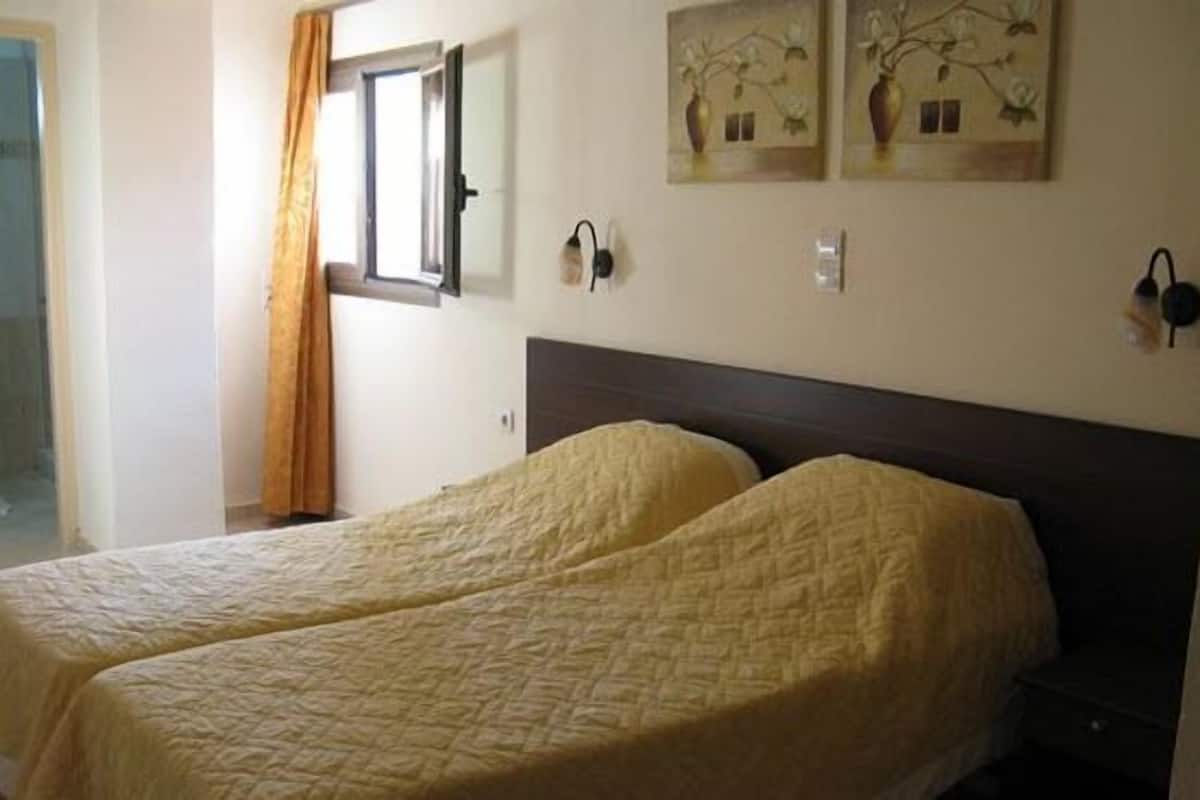 A room with two beds, a window with curtains, and wall-mounted lamps.