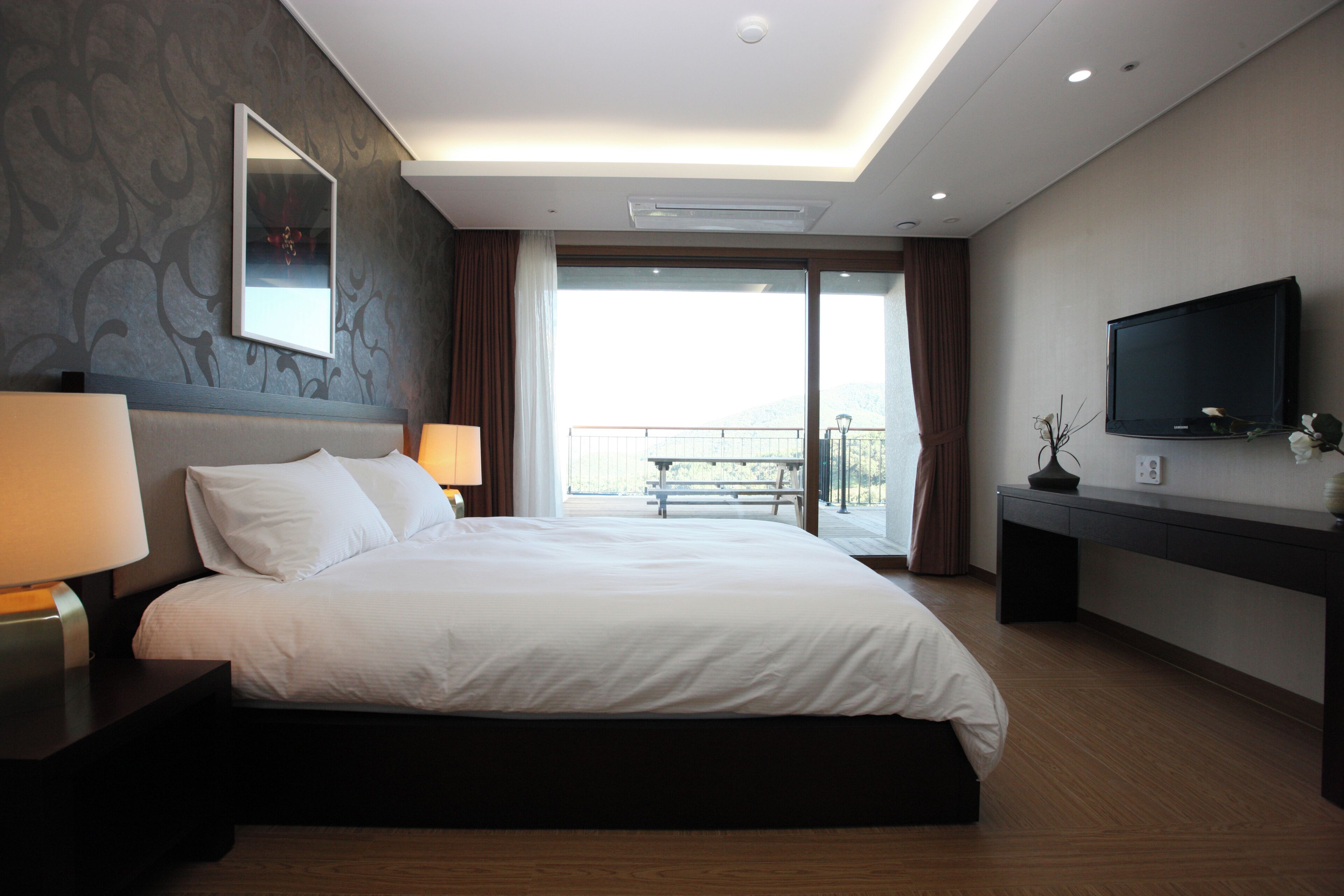 A hotel room with a large bed, two bedside lamps, a flat-screen TV, a balcony with a view, and a modern design.