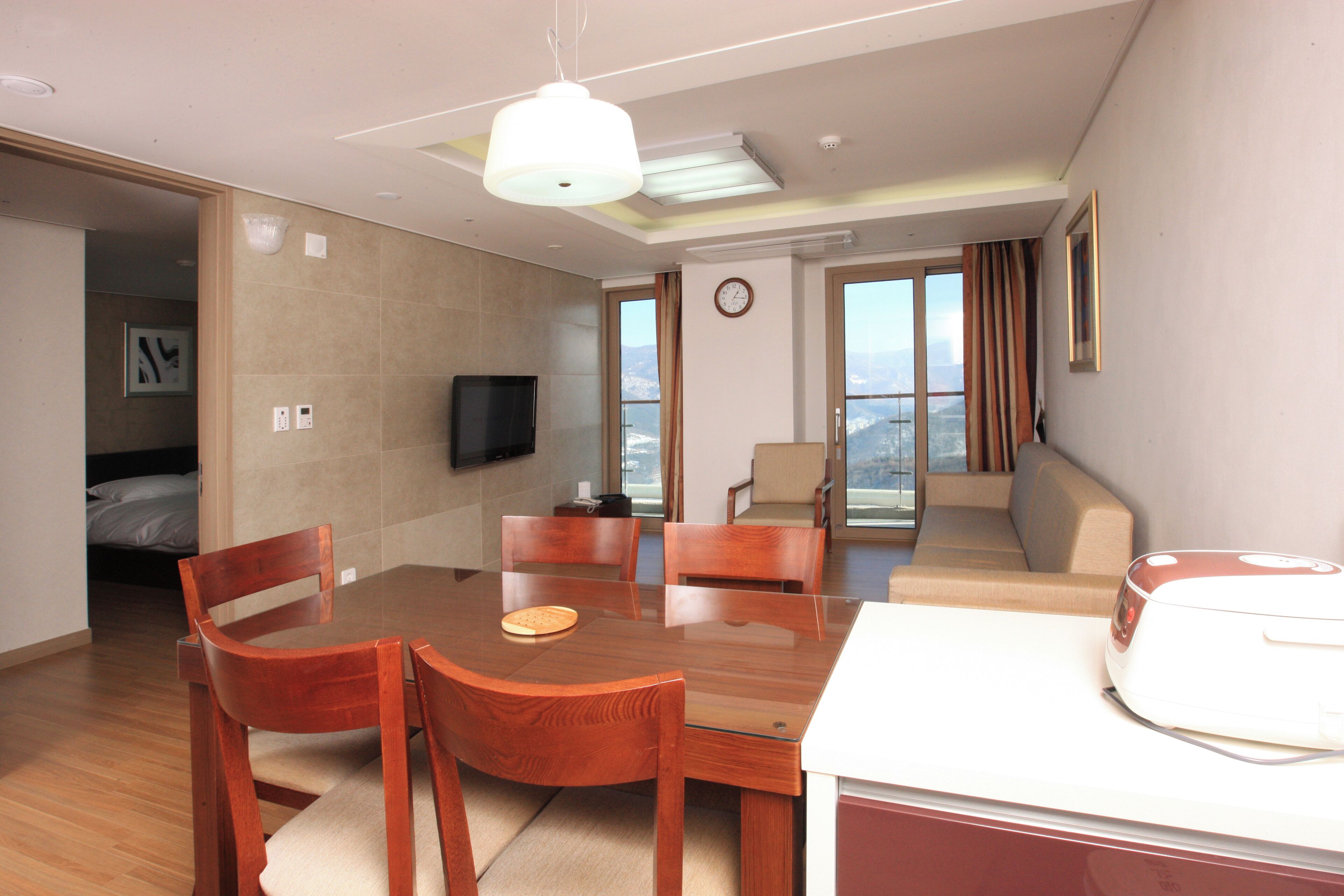 A hotel room with a dining table, chairs, a sofa, a TV, and a view of the city.