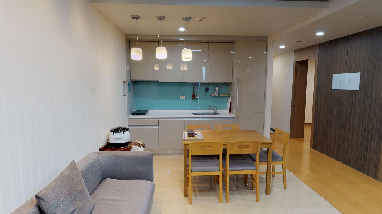 A modern kitchen with a dining area, featuring a wooden table and chairs, a built-in oven, and pendant lighting.