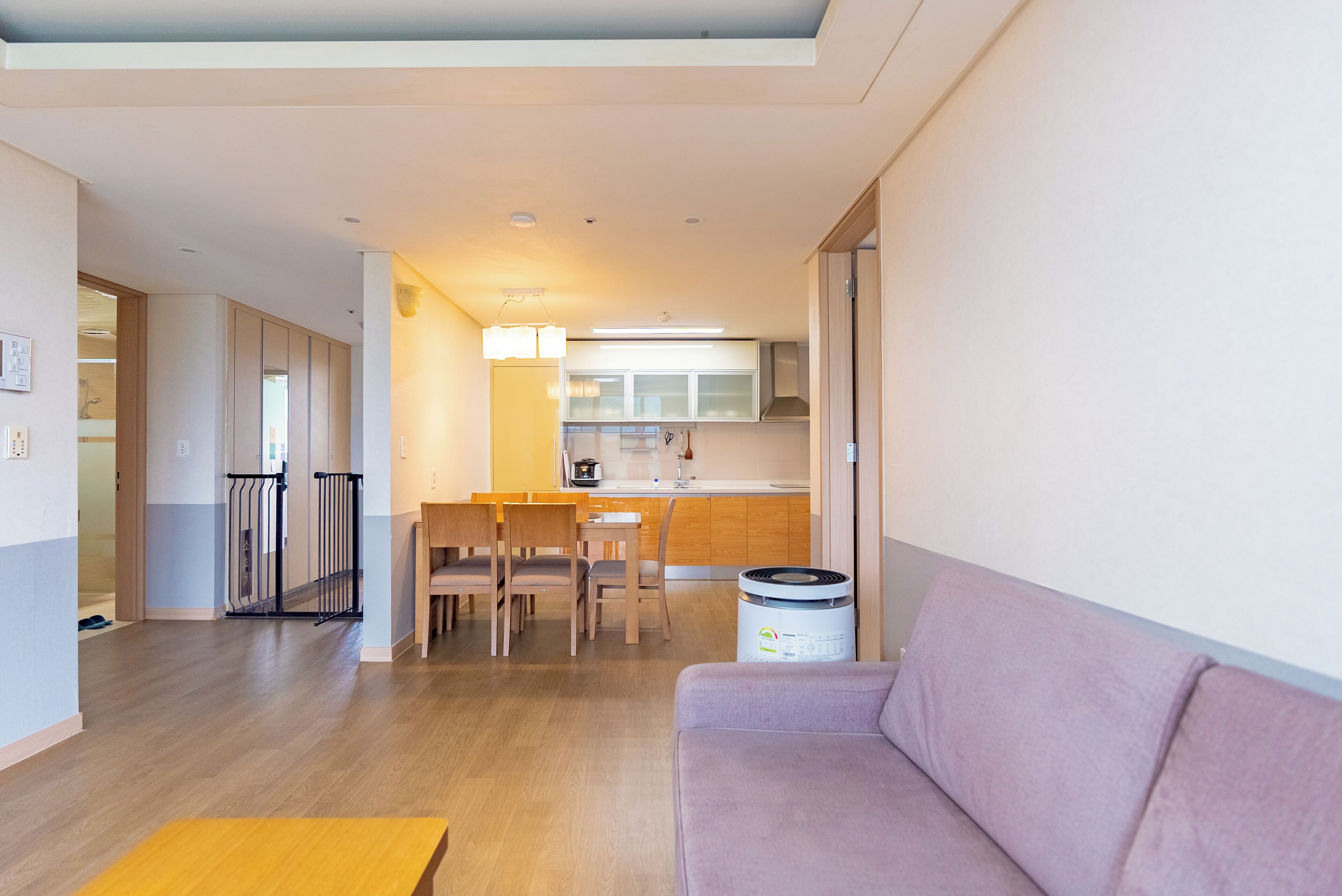 A modern living room with a sofa, a dining area with chairs, a kitchen with cabinets, and a trash bin.