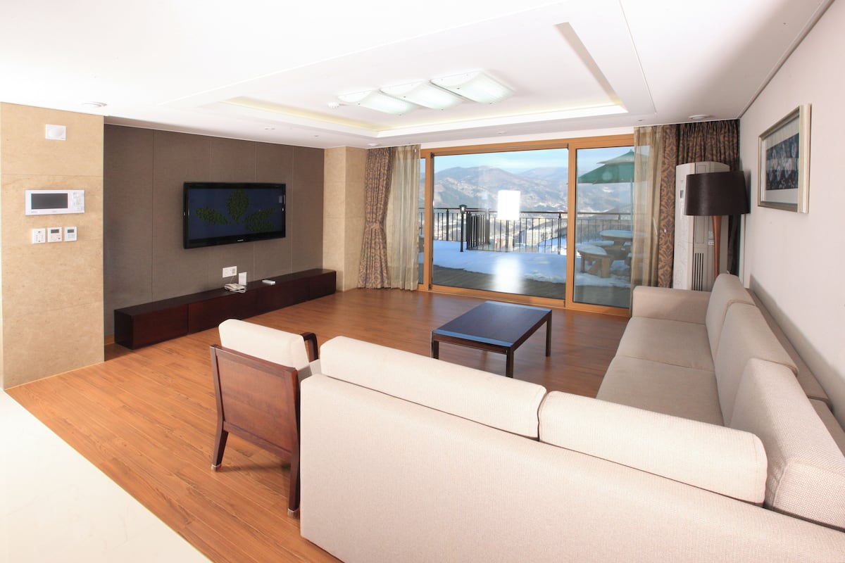 Ein modernes Wohnzimmer mit einer Couch, einem Couchtisch, einem Fernseher und einem Balkon mit Aussicht.