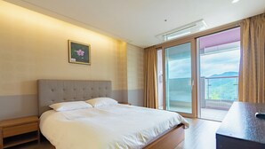 Ein Hotelzimmer mit Bett, Nachttisch, Schreibtisch und einer großen Glasschiebetür, die auf einen Balkon führt.