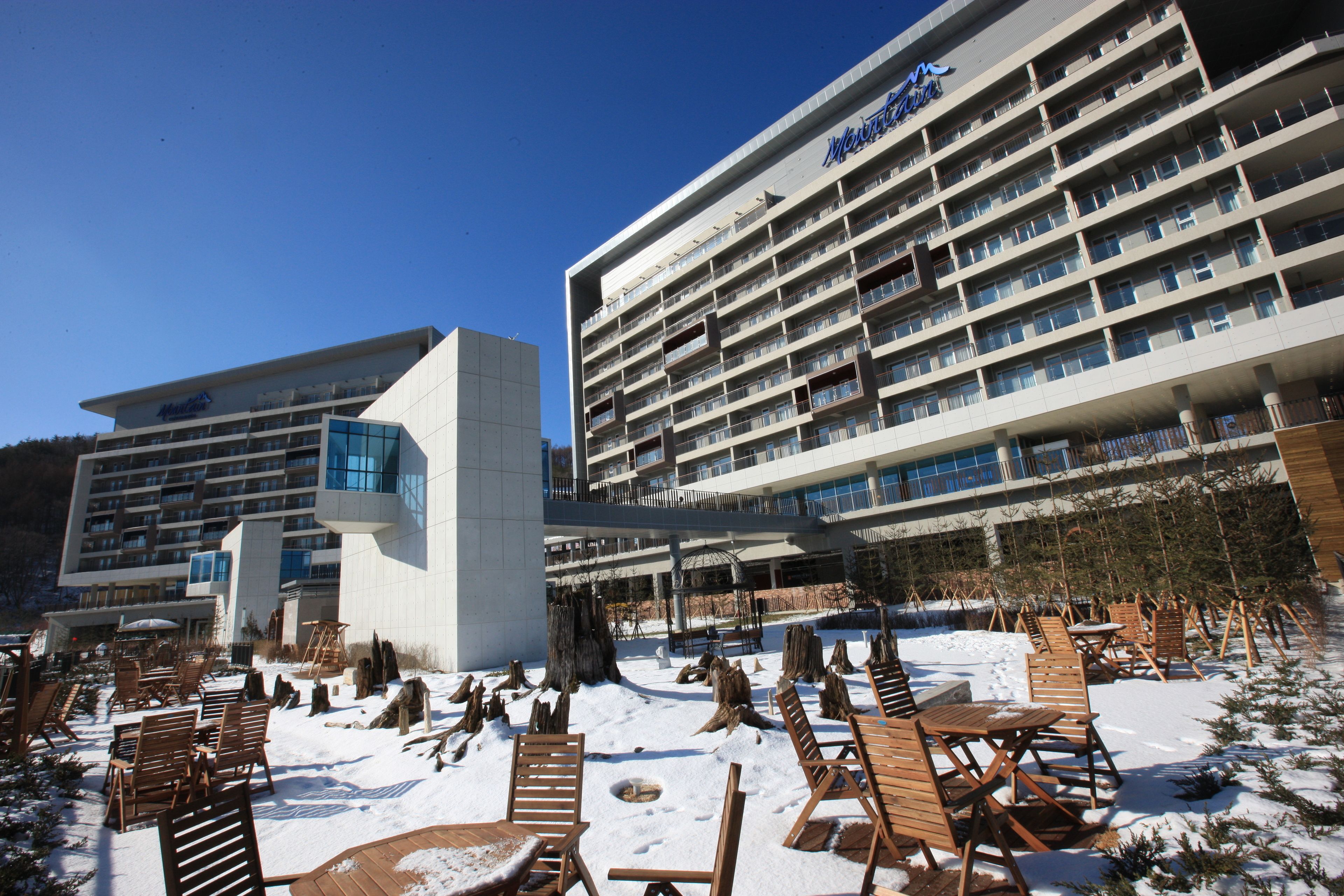 A hotel with multiple floors, outdoor seating, and snow on the ground.