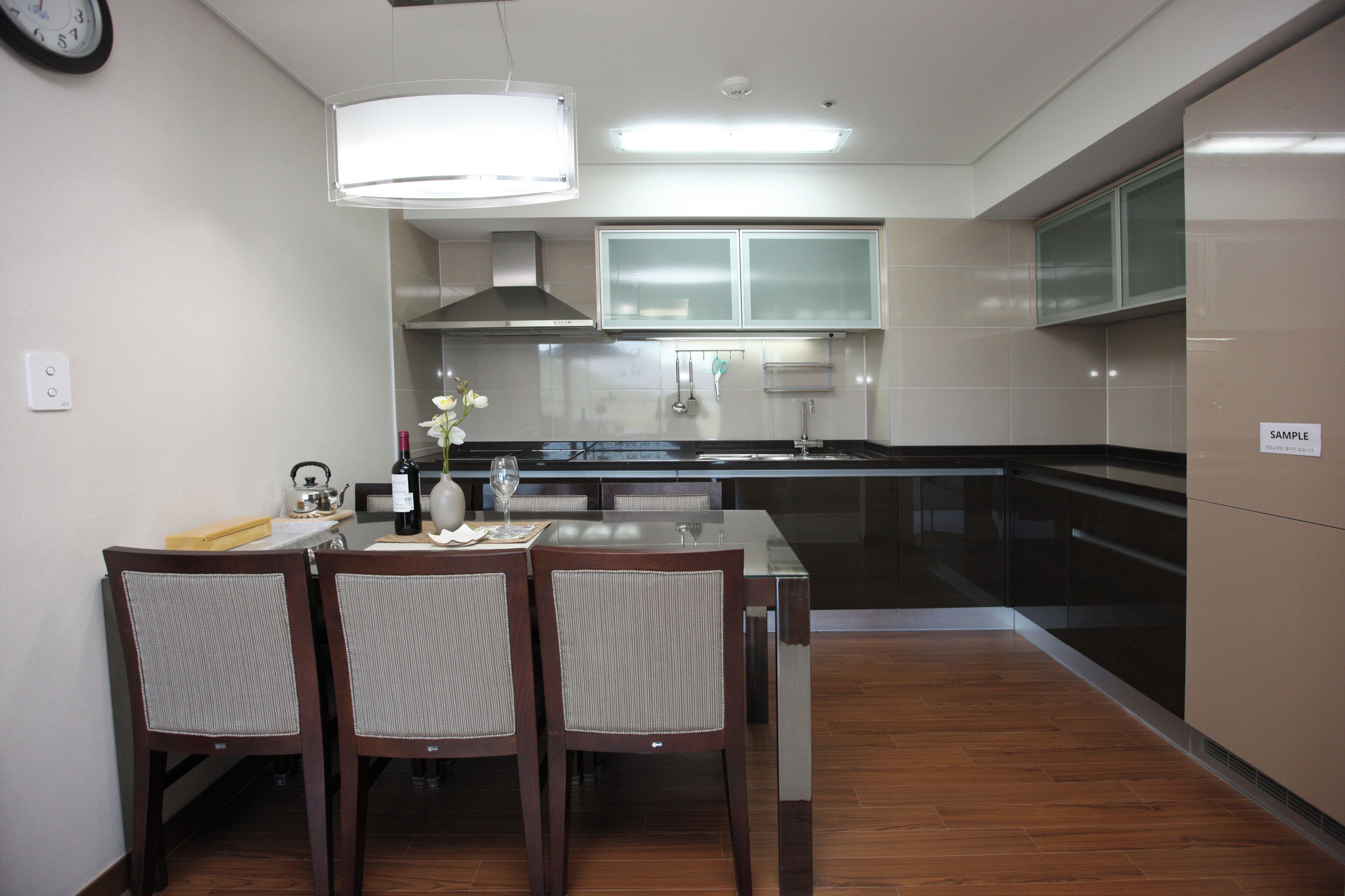 Una cocina moderna con comedor, que incluye una mesa con sillas, un reloj en la pared y un cartel que dice 'SAMPLE'.