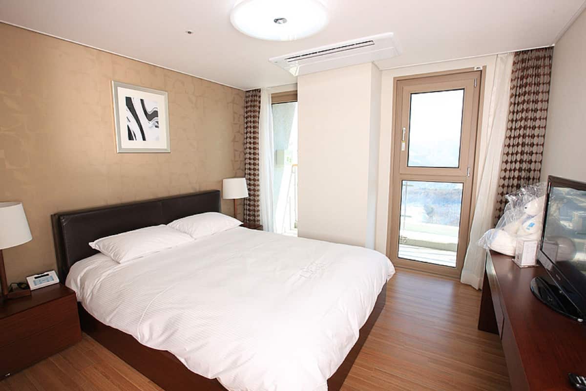 Ein Hotelzimmer mit einem großen Bett, einem Nachttisch mit Lampe, einem Fernseher und einem Fenster mit Vorhängen.