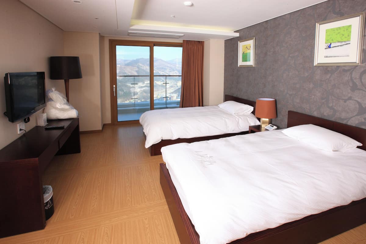 Ein Hotelzimmer mit zwei Betten, einem Fernseher, einem Schreibtisch und Blick auf die Stadt.
