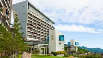 A modern hotel with multiple floors, a well-maintained lawn, and a view of mountains in the background.
